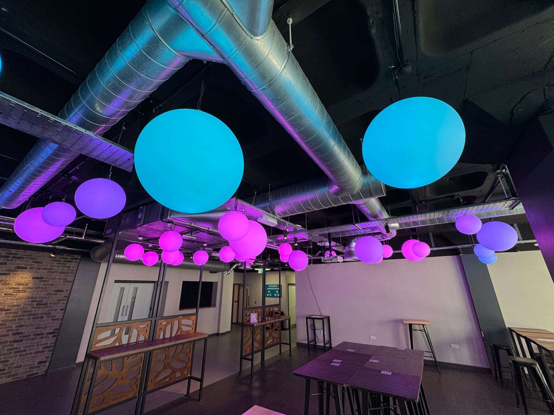 Exposed spiral supply ductwork above a lit leisure venue space
