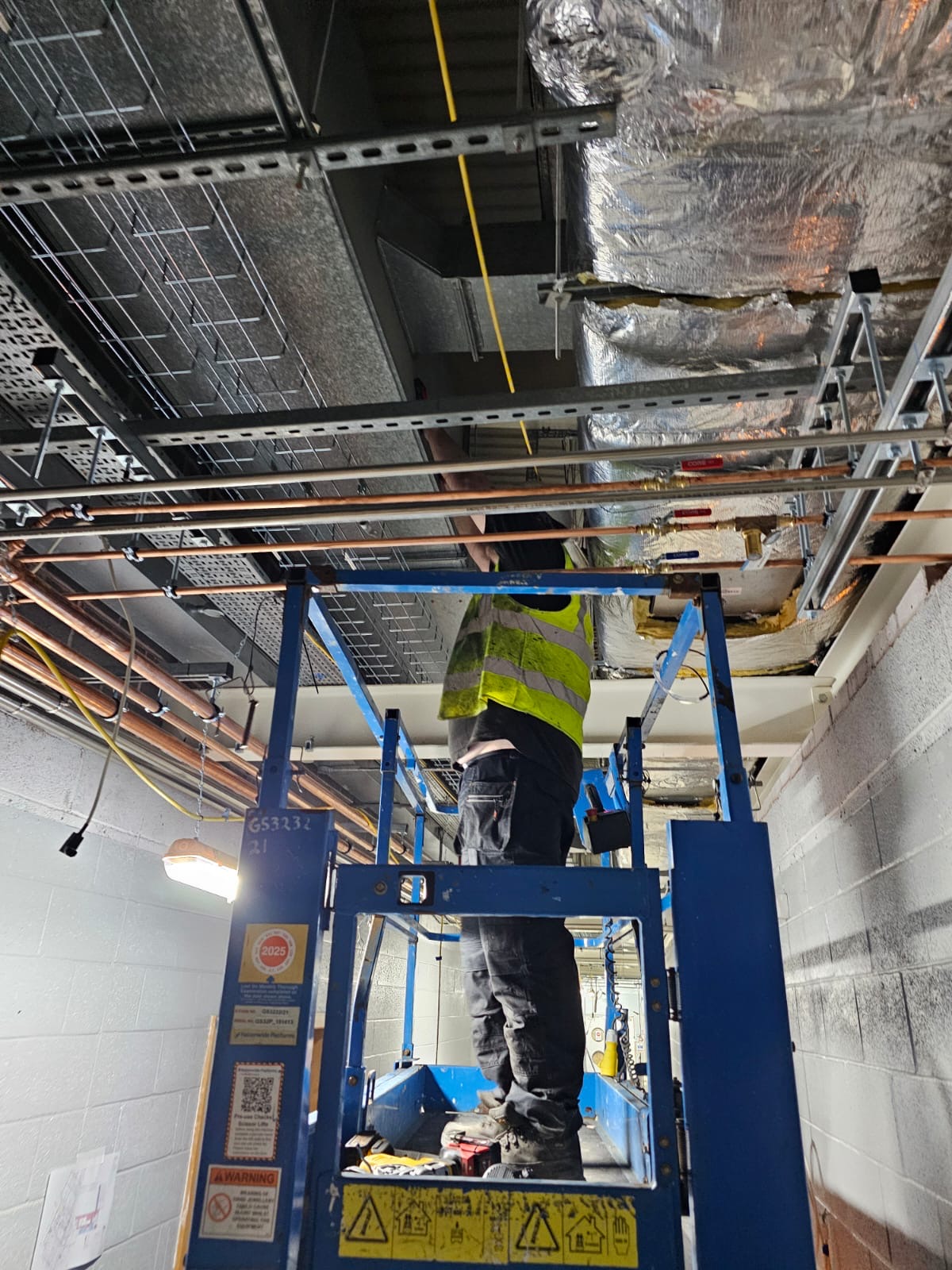 Deduct engineer on a scissor lift cleaning ceiling void ductwork in a UK office building